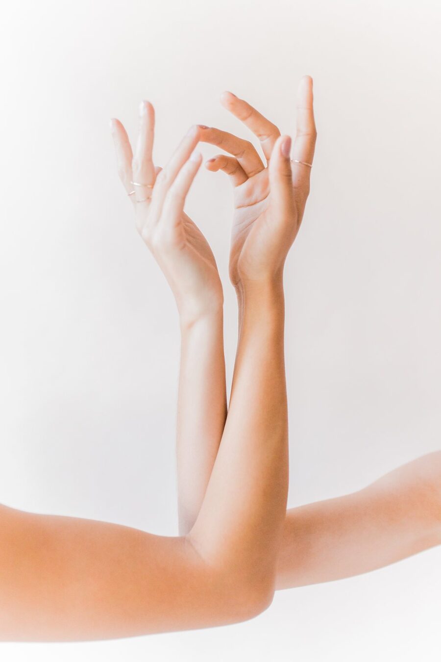 Two entwined hands with fingers pointing upward against a soft white background.