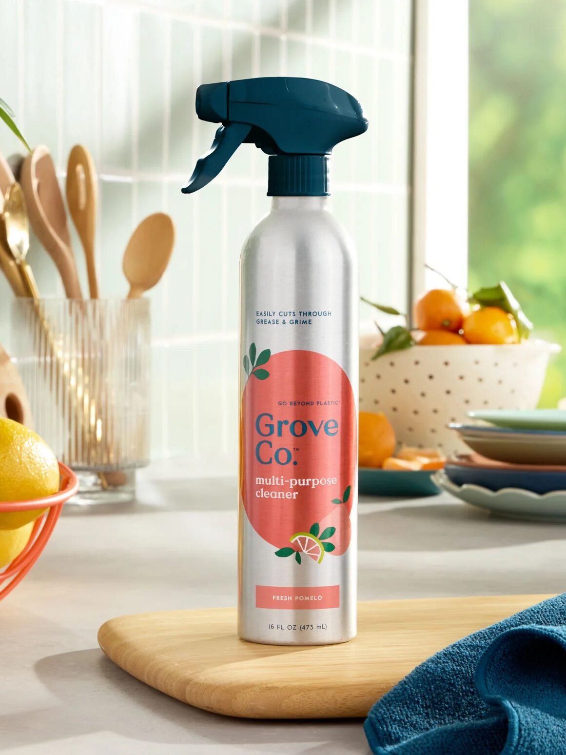 Spray bottle of Grove Co. multi-purpose cleaner on a wooden cutting board next to a blue cloth in a kitchen setting.