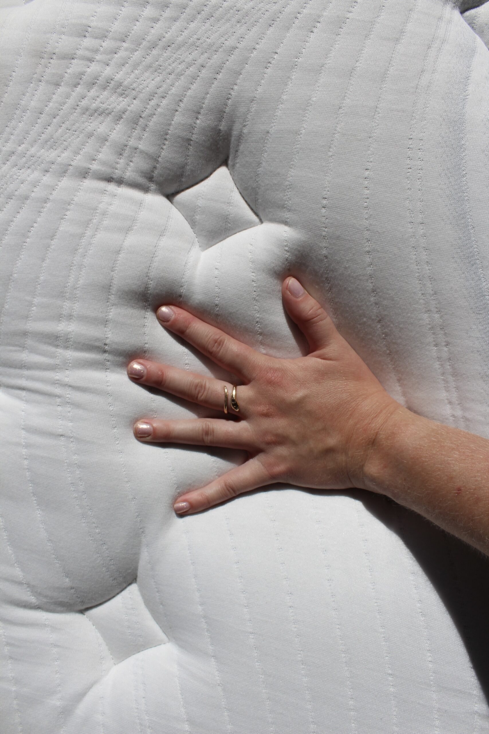 Emily McGowan's hand, adorned with a gold ring, presses into the white, quilted Bear Elite Pro mattress, demonstrating the texture and softness of this nontoxic mattress.