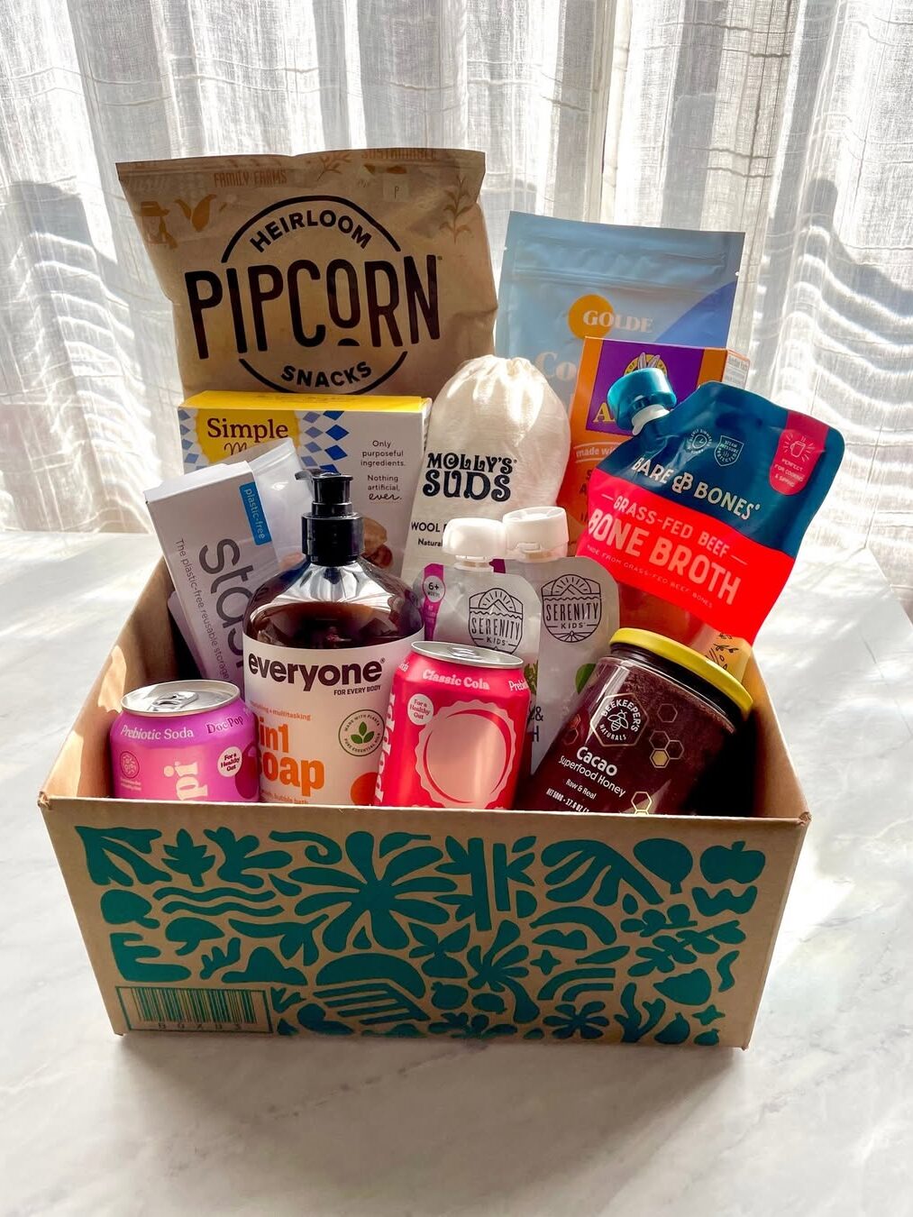 A gift box on a table containing snacks, soap, detergent, supplements, and other wellness products.