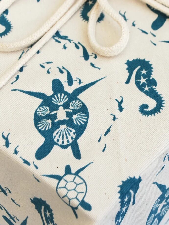A fabric-wrapped box featuring blue sea turtle, seahorse, and fish patterns on a beige background with a beige rope tied around it.