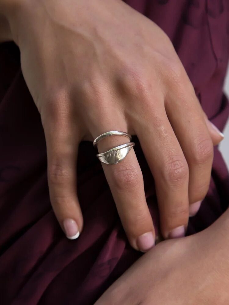 Hand wearing a silver, double-banded ring resting on a person's maroon outfit.