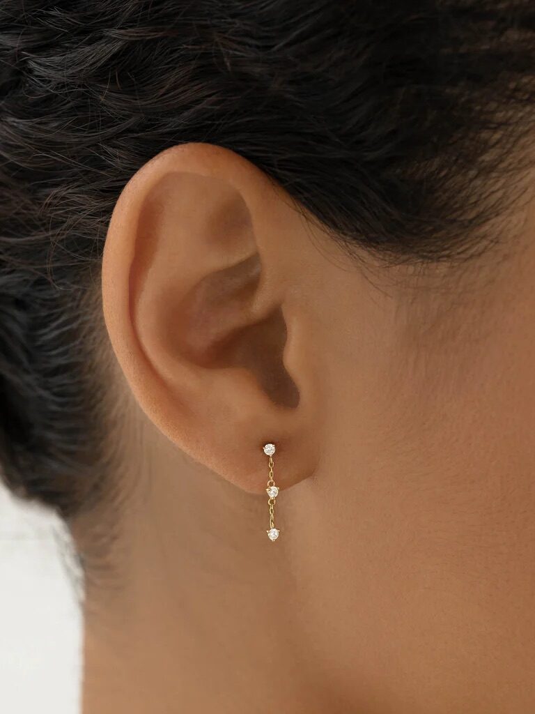 Close-up of a woman's ear wearing a delicate gold drop earring with a small gemstone at the end.