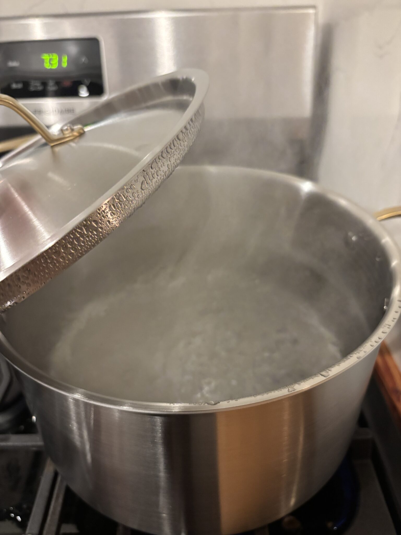 A large stainless steel pot of water boiling on a stove, with steam rising and the lid partially lifted.