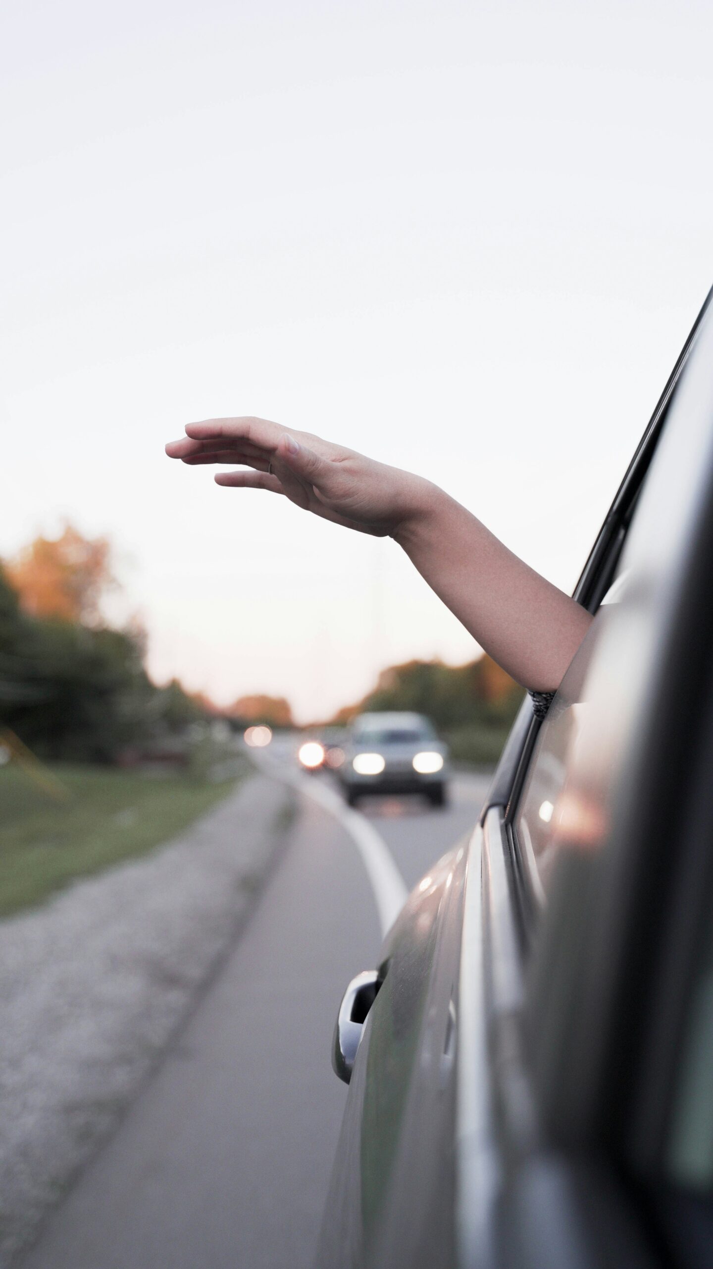 A hand extends out of a car window on a road with other vehicles in the background during daylight.