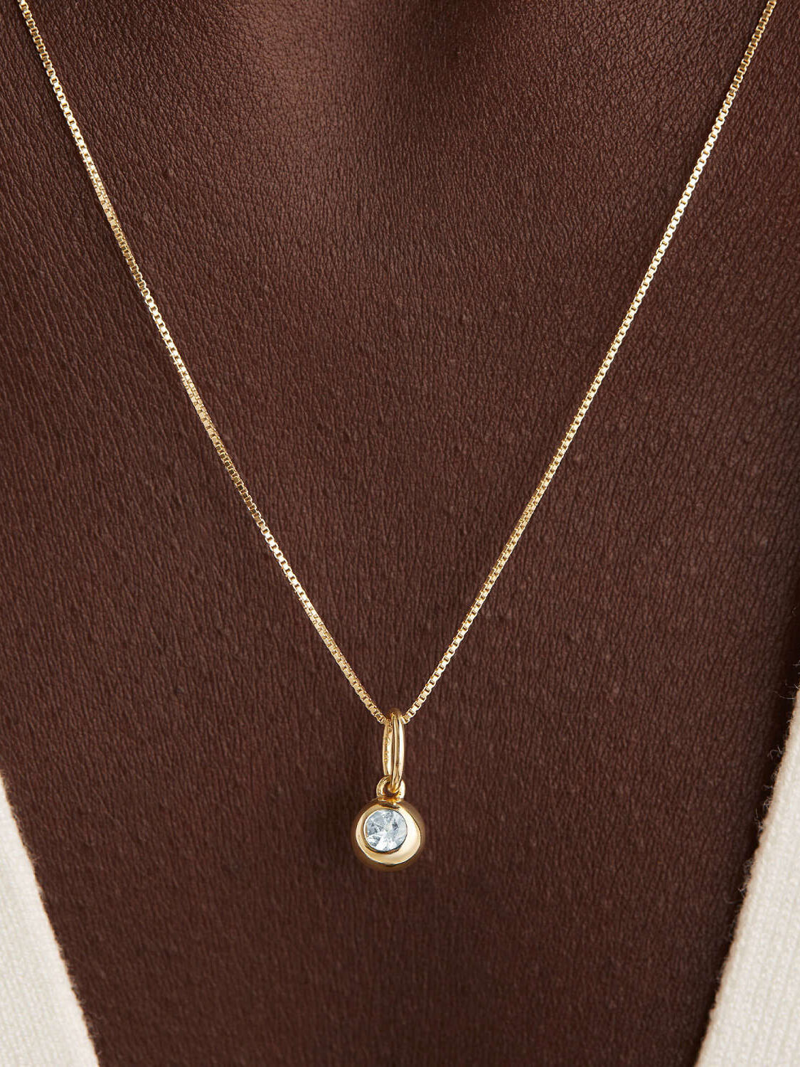 Gold necklace with a single pendant on a person wearing a white top.
