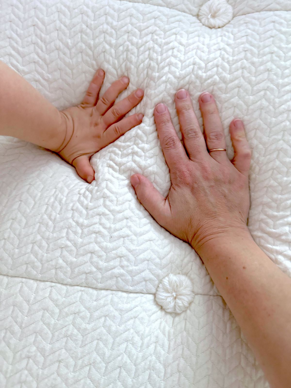 Reviewer Stephanie Fallon and her child's hand press down on a textured, nontoxic mattress from My Green Mattress, highlighting its safety for families.