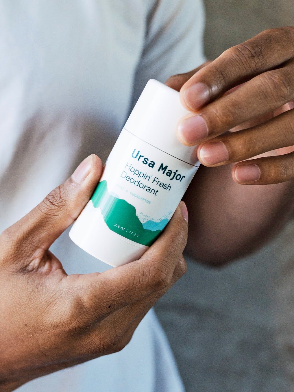 A person holding a stick of "Ursa Major Hoppin' Fresh Deodorant" with both hands, against a plain background.