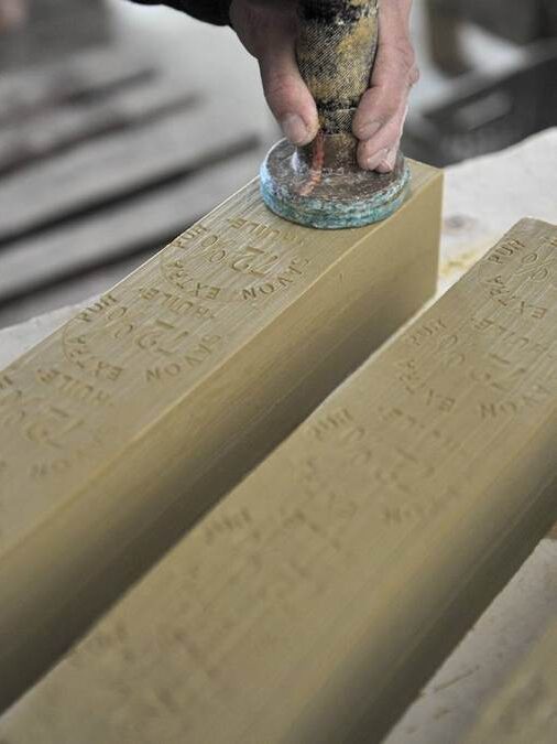 A person stamps text onto large rectangular bars of soap with a round metal tool.