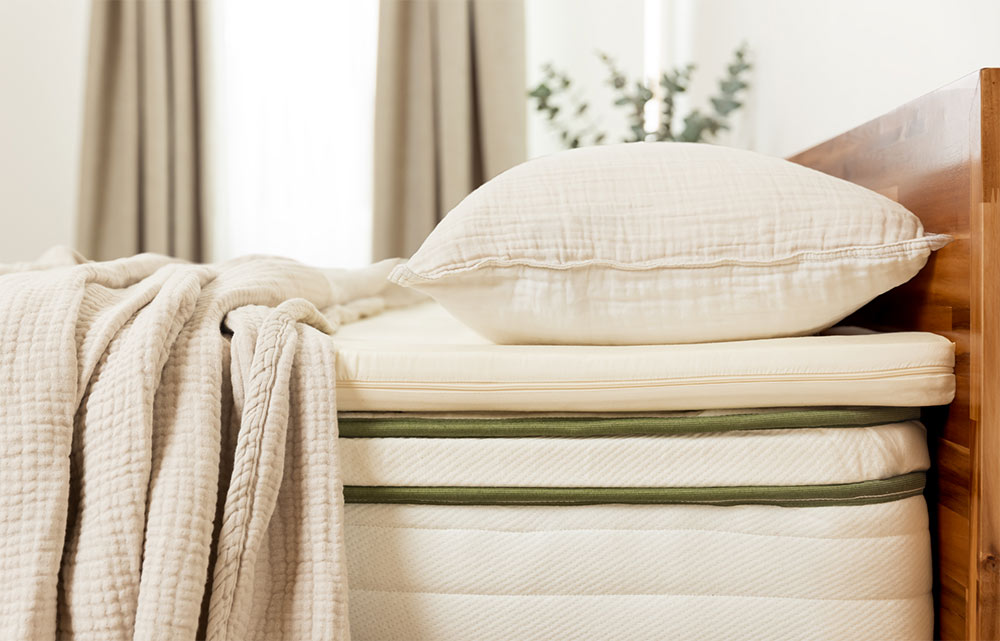 Pillow and textured beige blanket on a neatly made bed with a light-colored mattress in a well-lit bedroom.