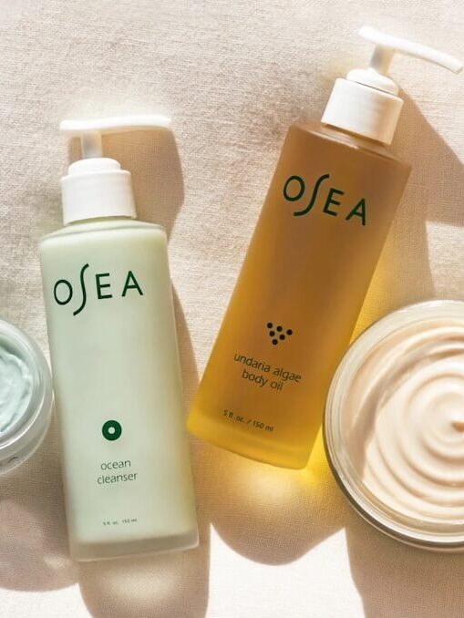 Two OSEA bottles: an ocean cleanser and undaria algae body oil, positioned on a light fabric alongside a jar of cream.
