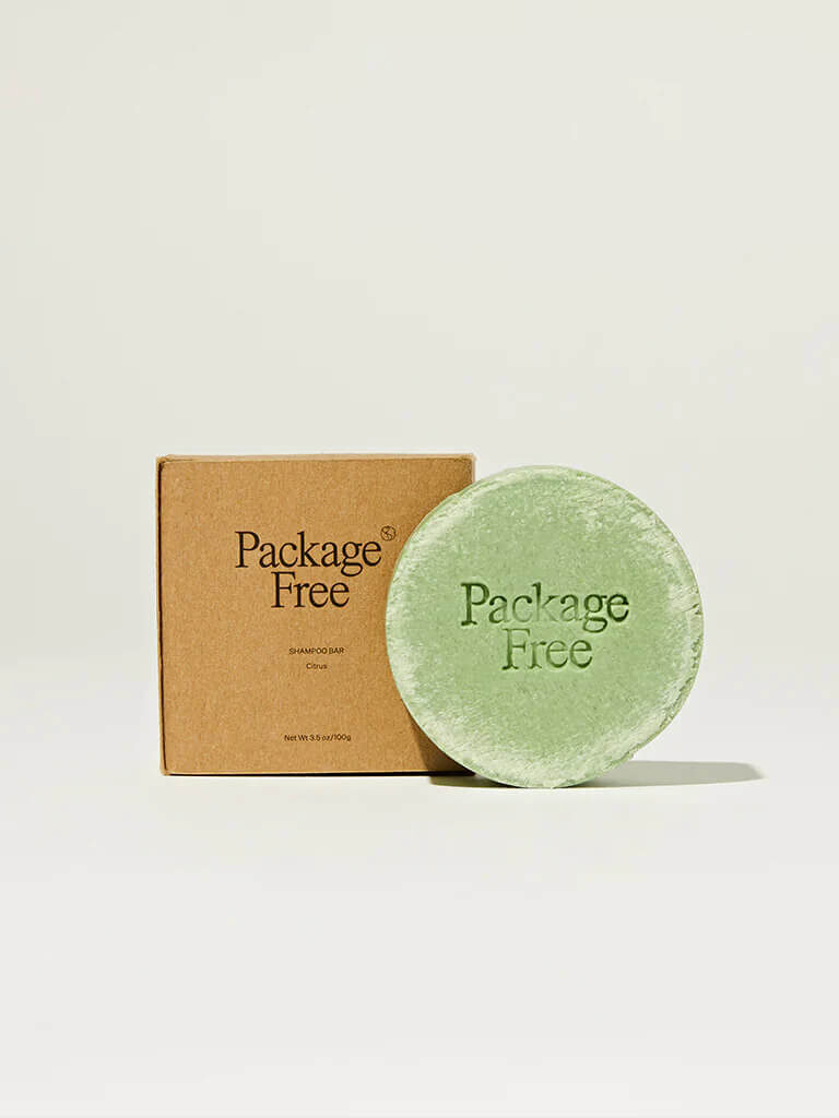 A Package Free shampoo bar that's circular and green next to it's cardboard box packaging. 
