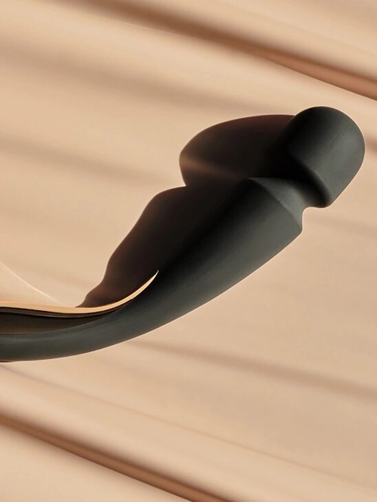 A black, curved massage device with a bulbous end is placed on a beige surface with soft shadows.