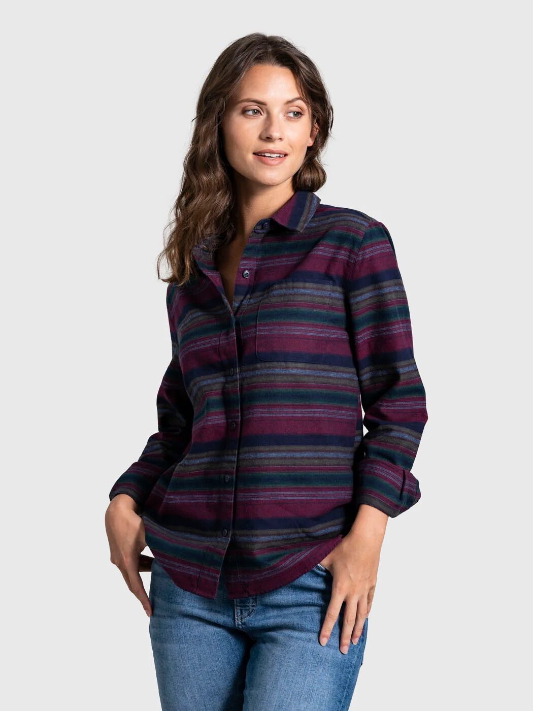 A person wearing a striped, multicolored button-up shirt and jeans stands against a plain background.