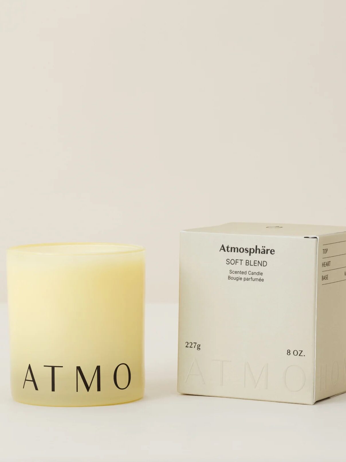 A cream-colored candle in a glass holder labeled "ATMO" is placed next to its matching box, which reads "Atmosphère Soft Blend Scented Candle, 8 oz, 227g.
