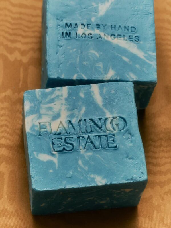Two blue marbled soap bars on a tan surface; one is embossed with "FLAMINGO ESTATE" and the other with "MADE BY HAND IN LOS ANGELES.