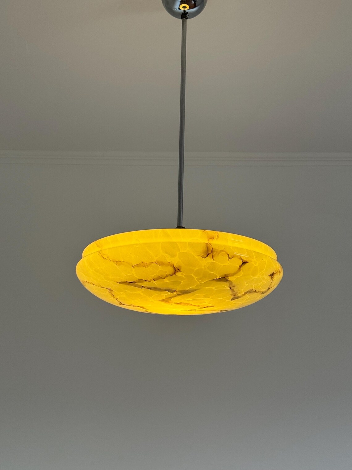 A circular, yellow marbled ceiling light fixture hangs from a black rod against a plain gray ceiling background.