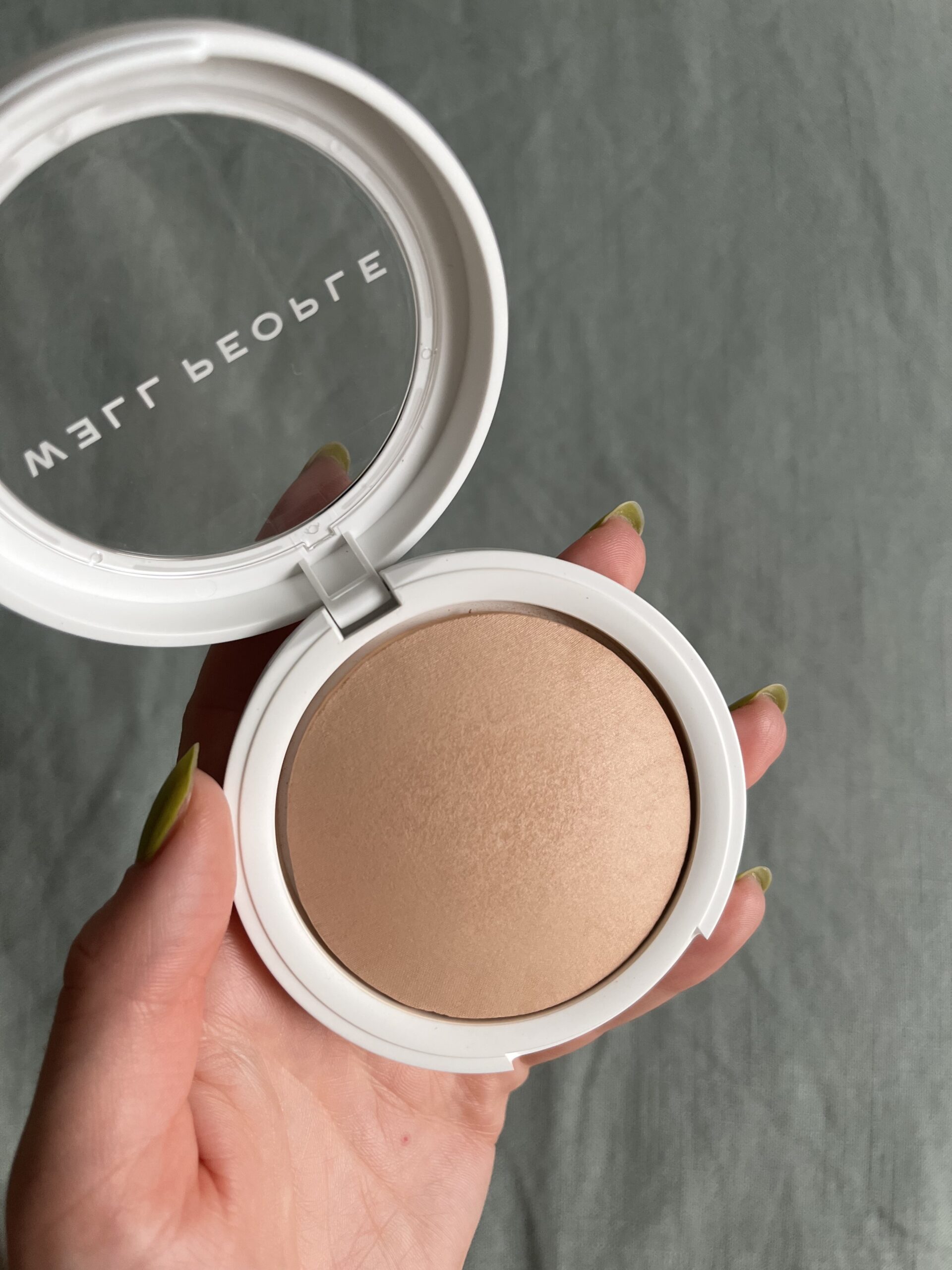 A hand holds a Well People powder foundation compact open.