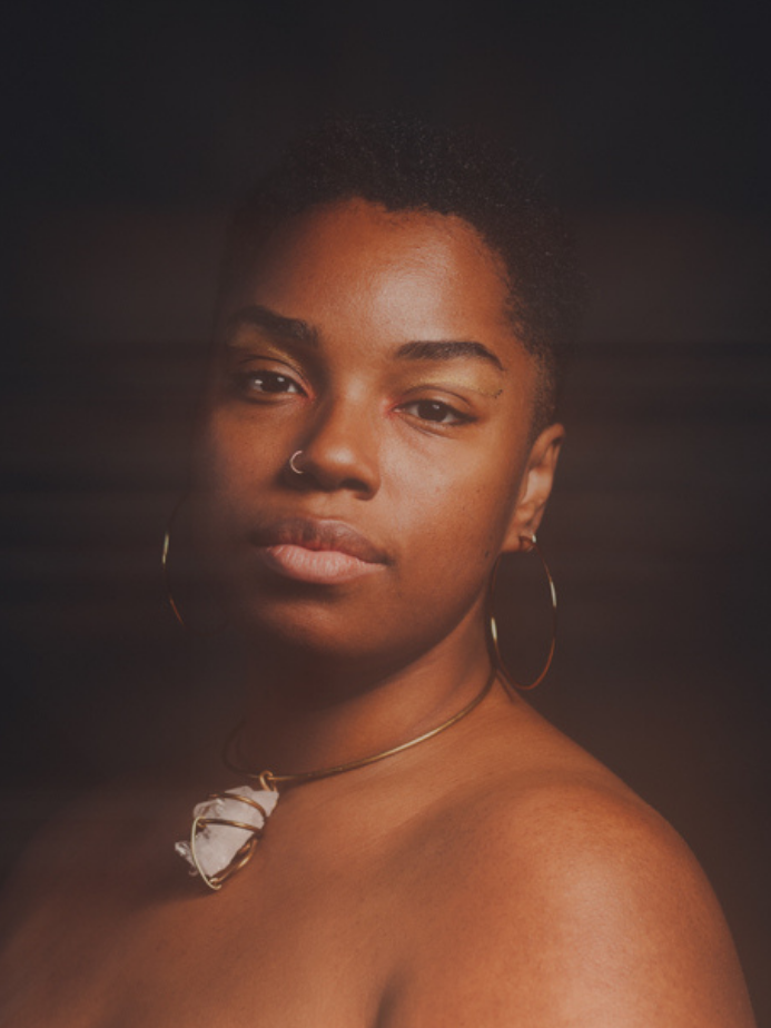 A person with short hair and hoop earrings poses beside text that reads "SHINE out now" on a dark background.