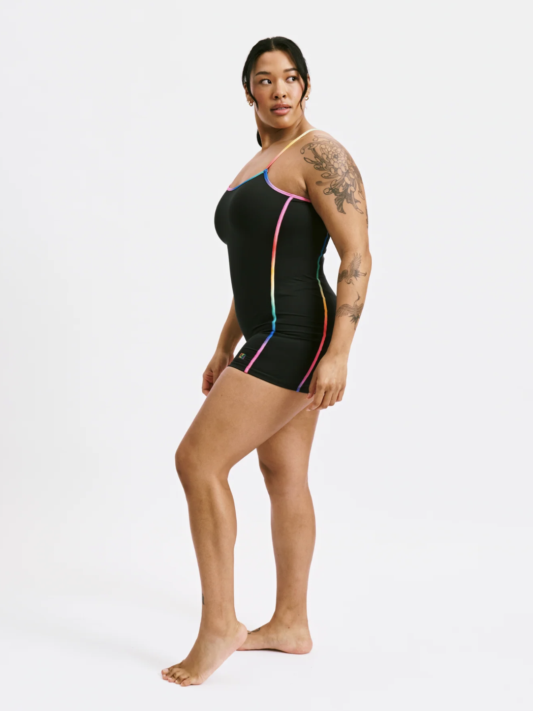 Person in a black fitted tank unitard with colorful trim stands barefoot on a plain white background.