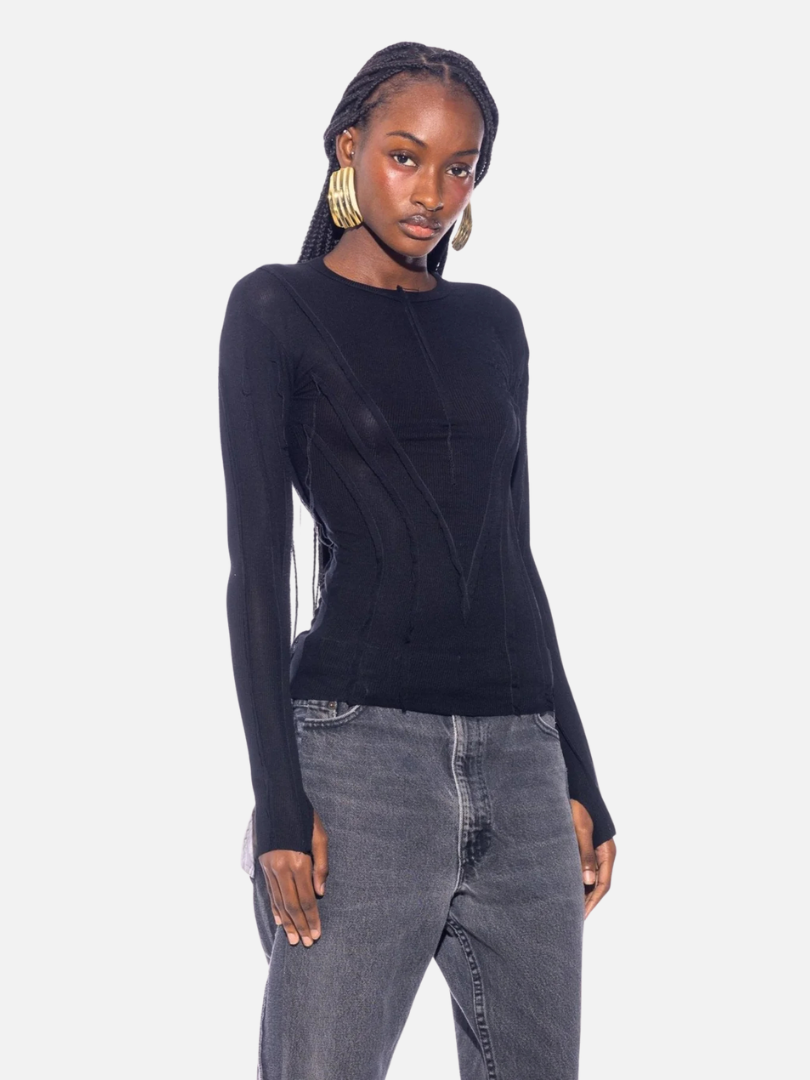 Person wearing a black long-sleeve top, gray jeans, and large hoop earrings against a plain background.