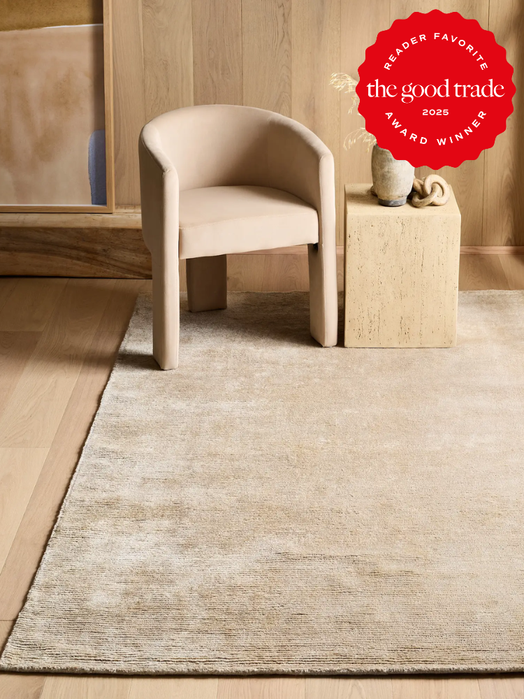 A beige armchair and stone side table sit on a light-colored rug in a minimalist room with wood panel walls; a "The Good Trade Award Winner 2023" badge is in the top right corner.