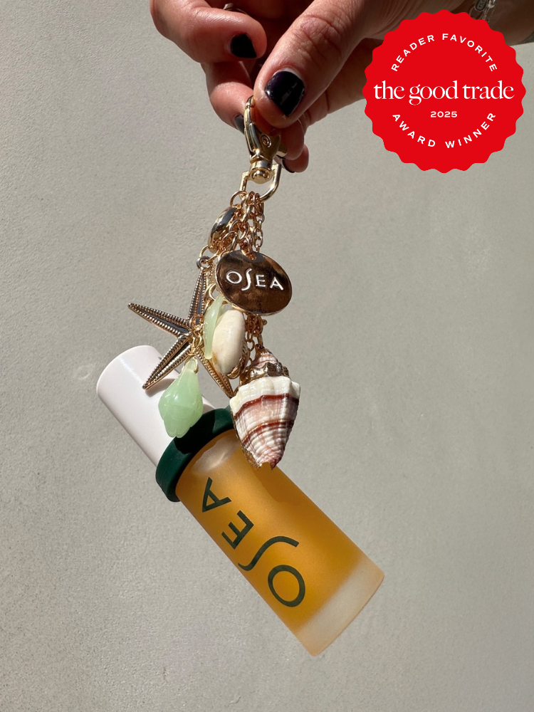 A hand holds a keychain with a starfish, shell charms, and an OSEA bottle. A red badge in the corner reads "The Good Trade, Reader Favorite, Award Winner 2024.