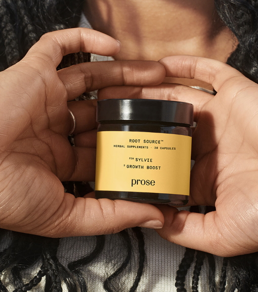A person holds a jar labeled "Root Source Growth Boost" herbal supplements by Prose, with a yellow label and black lid.