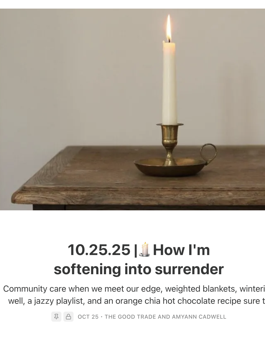 A single white candle in a brass holder sits on a wooden table against a plain, light-colored wall.