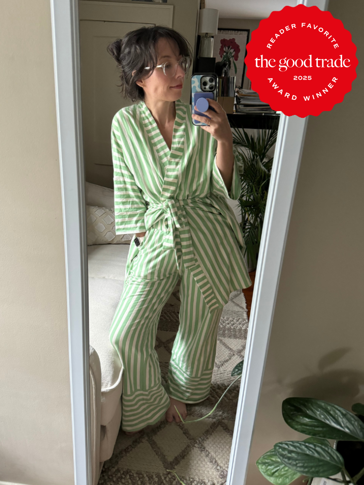 Person in a green and white striped pajama set takes a mirror selfie in a room with plants and a rug. Red award badge in corner.