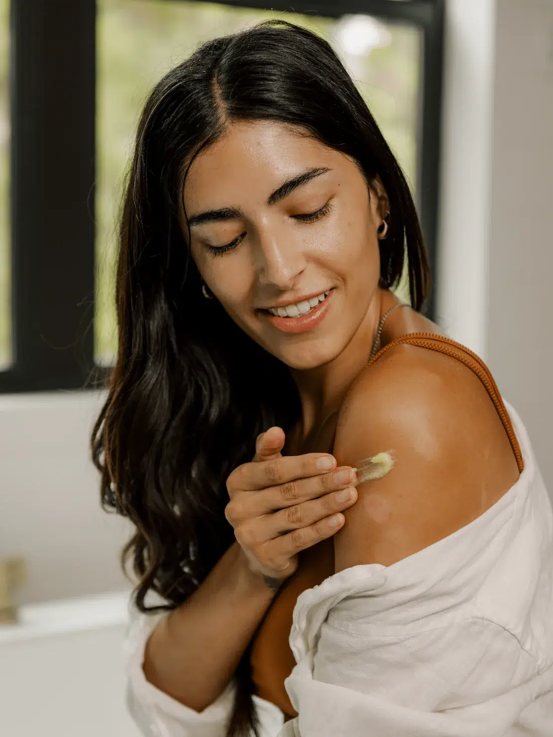 Person applying cream to their shoulder while smiling, indoors.