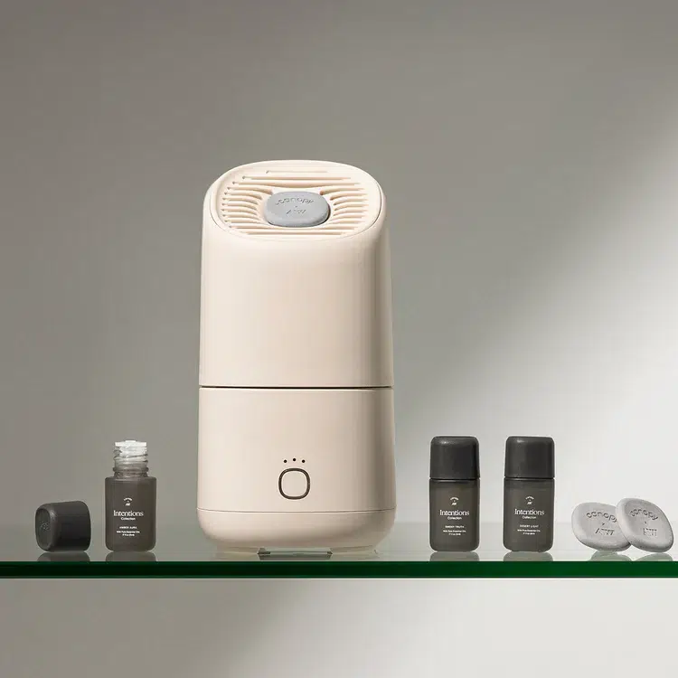 A beige air purifier or diffuser with a button on the front is placed on a glass surface, surrounded by small bottles and capsules labeled "keyoon.